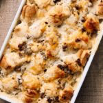 Creamy chicken and mushroom casserole baked with flaky puff pastry, topped with melted cheese, served in a white ceramic dish on rustic wooden table.