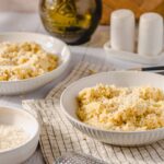 Creamy mashed potatoes with grated cheese in white bowls on a rustic kitchen table. Freshly cooked mashed potatoes topped with cheese, perfect for comfort food, side dishes, or family meals.