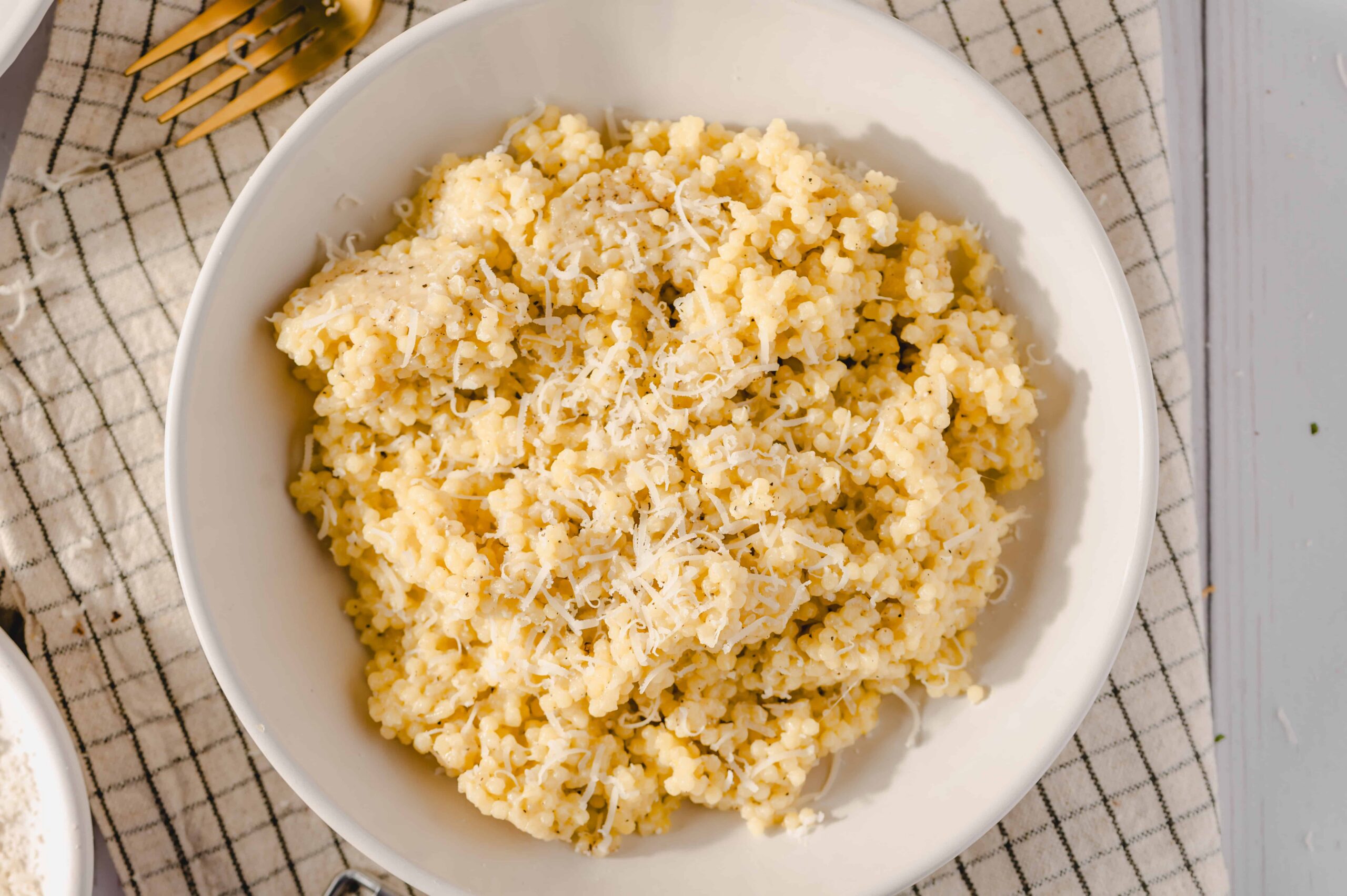 Creamy cheese mashed potatoes with shredded cheese on top, served in a white bowl on a checkered tablecloth. Perfect comfort food for dinner or holiday meals.