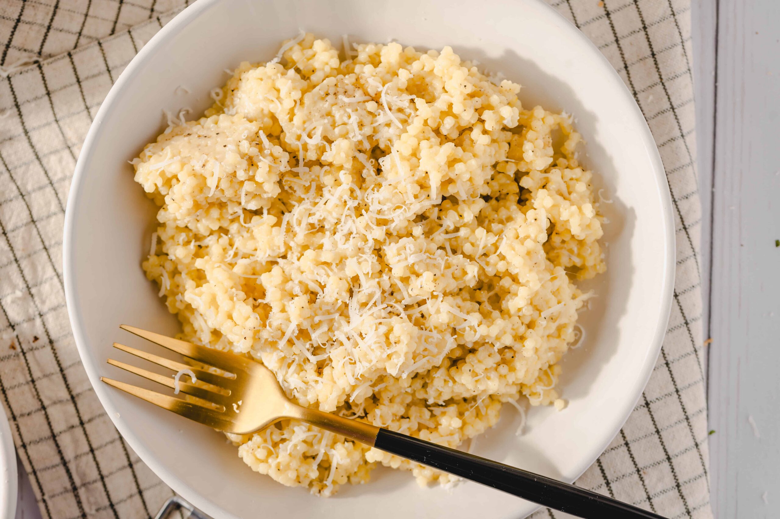 Creamy grated cheese on fluffy mashed potatoes served on a white plate, garnished with shredded cheese, with a gold fork on the side, perfect comfort food.