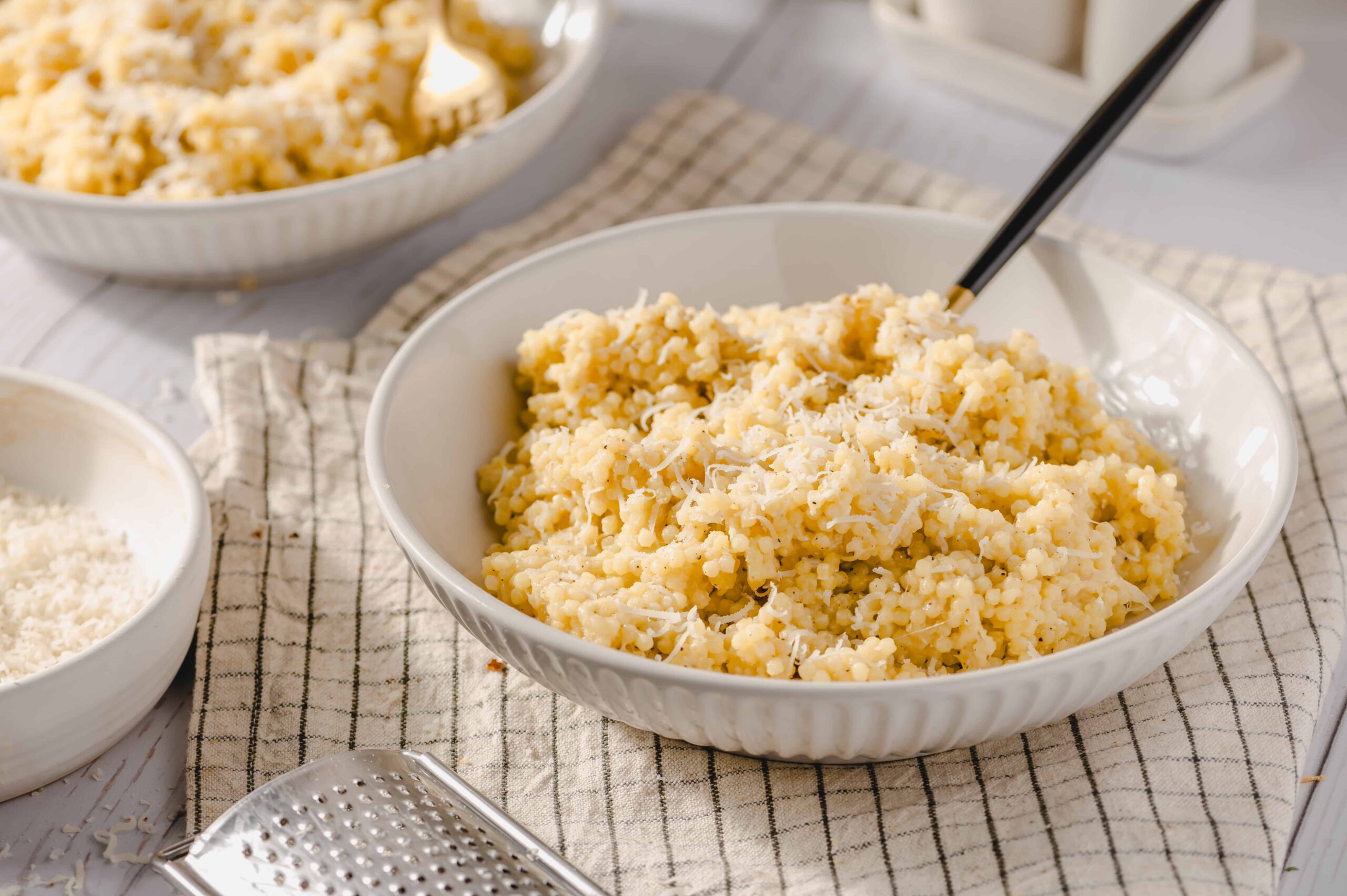 Creamy shredded cheese pasta in a white bowl with grated cheese and additional bowls of cheese nearby, on a rustic kitchen setup for a delicious homemade meal.