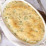 Creamy baked casserole with bread crumbs, green peas, and melted cheese, served in an oval dish for a delicious comfort food meal.