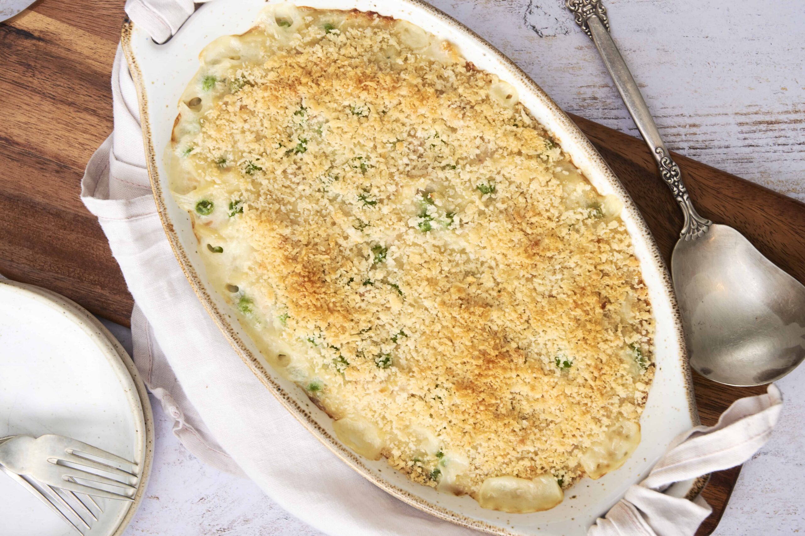 Creamy baked casserole with bread crumbs, green peas, and melted cheese, served in an oval dish for a delicious comfort food meal.