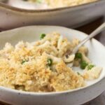 Creamy baked macaroni and cheese topped with a crunchy breadcrumb crust, served in a rustic white bowl with fresh green peas, perfect comfort food for all ages.