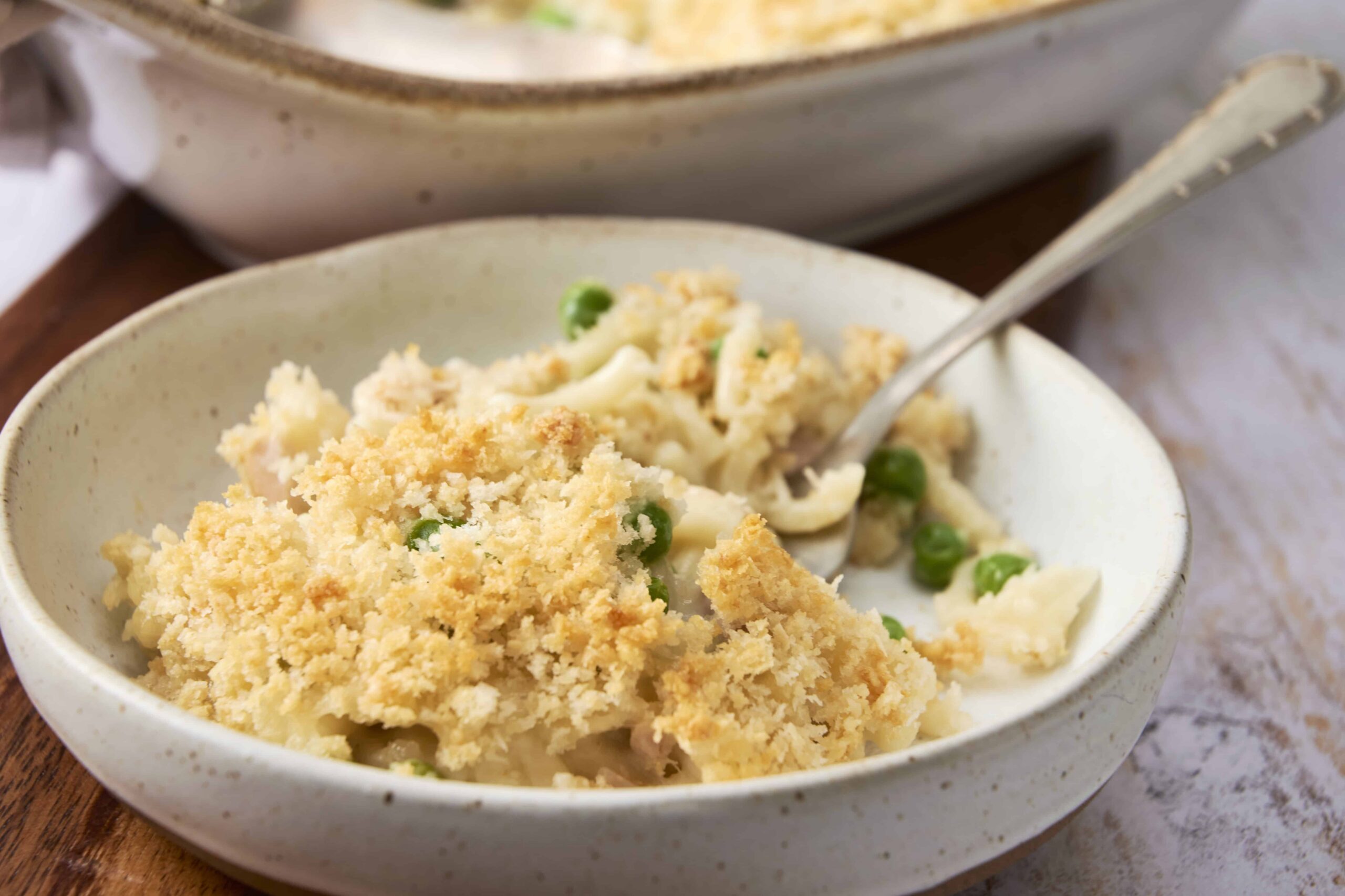 Creamy baked macaroni and cheese topped with a crunchy breadcrumb crust, served in a rustic white bowl with fresh green peas, perfect comfort food for all ages.