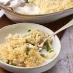 Creamy cauliflower casserole with peas and crispy breadcrumb topping served in a rustic white bowl, perfect for comforting side dishes and family dinners.
