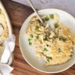 Creamy chicken pot pie filling topped with peas and crispy breadcrumbs in a ceramic bowl, served on a wooden surface, highlighting comfort food and homemade pie ingredients.