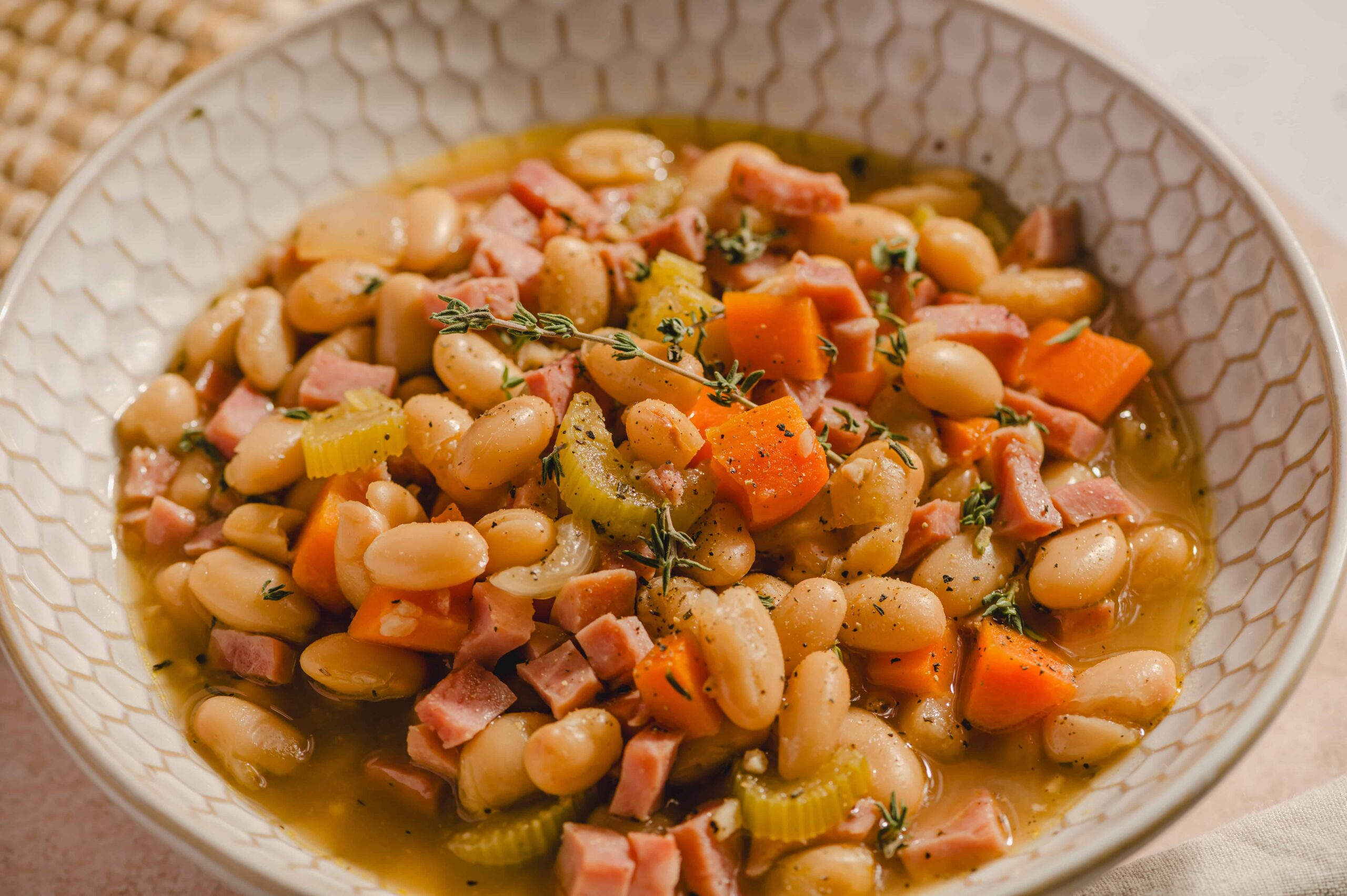 Creamy white beans and ham stew with carrots and herbs in a white textured bowl for hearty comfort food.