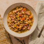 Creamy white bean and ham soup with vegetables in a decorative bowl on a light pink surface.