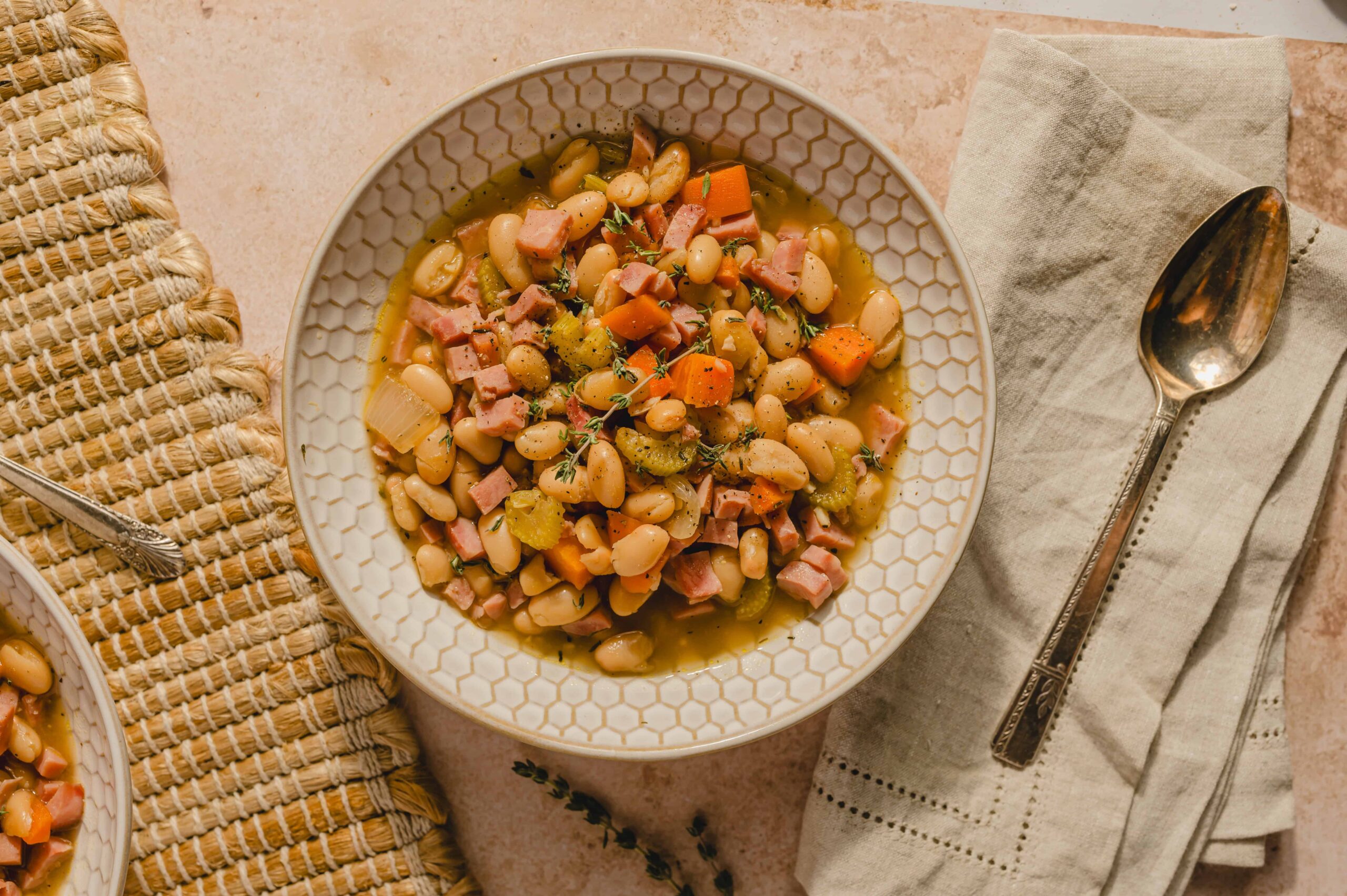 Creamy white bean and ham soup with vegetables in a decorative bowl on a light pink surface.