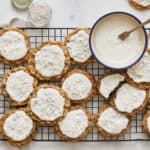 Buttery oatmeal cookies topped with white icing and festive sprinkles on a cooling rack. Perfect holiday treats for Christmas or any celebration. Easy homemade cookie recipe with simple ingredients.