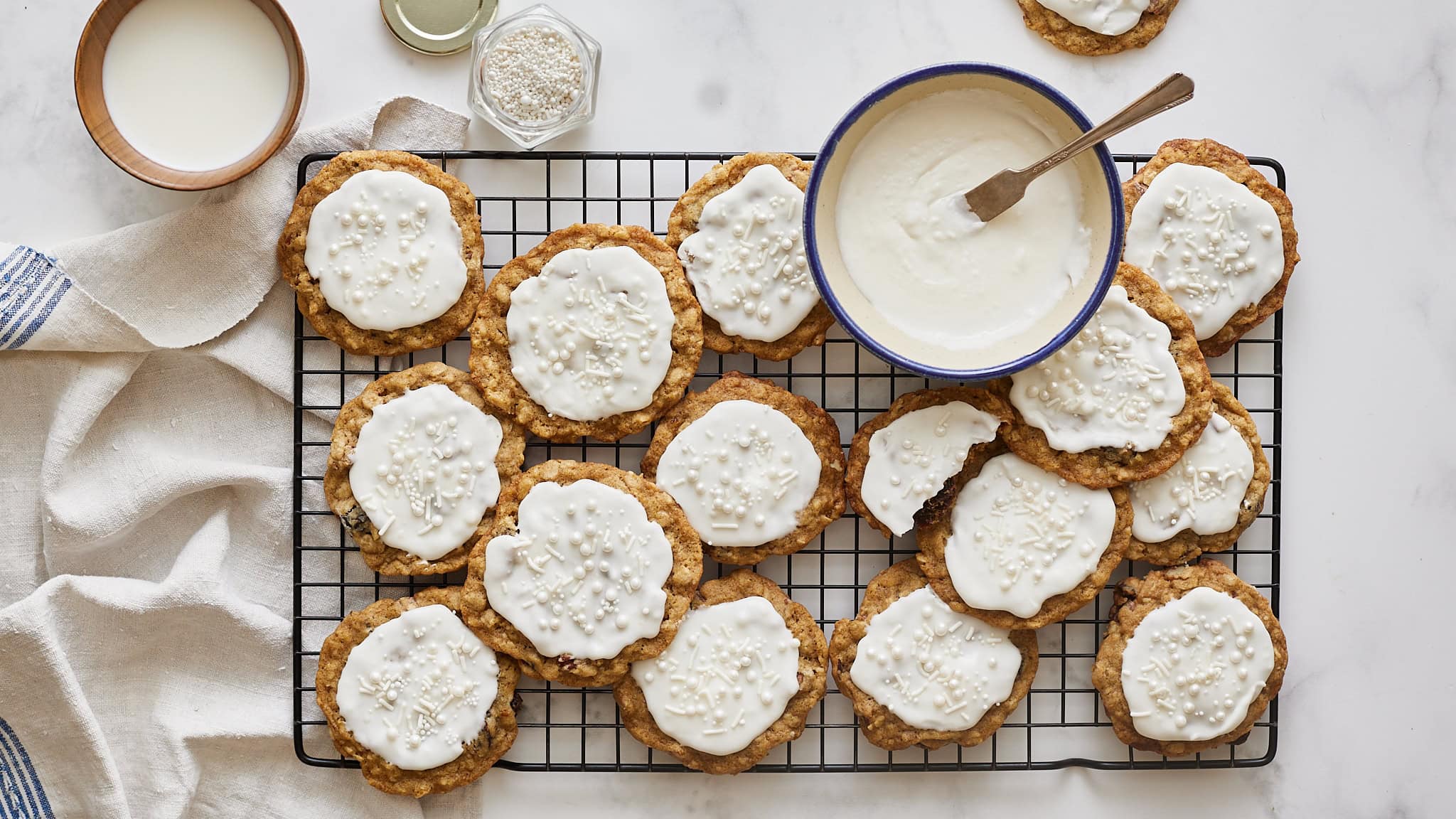 Buttery oatmeal cookies topped with white icing and festive sprinkles on a cooling rack. Perfect holiday treats for Christmas or any celebration. Easy homemade cookie recipe with simple ingredients.