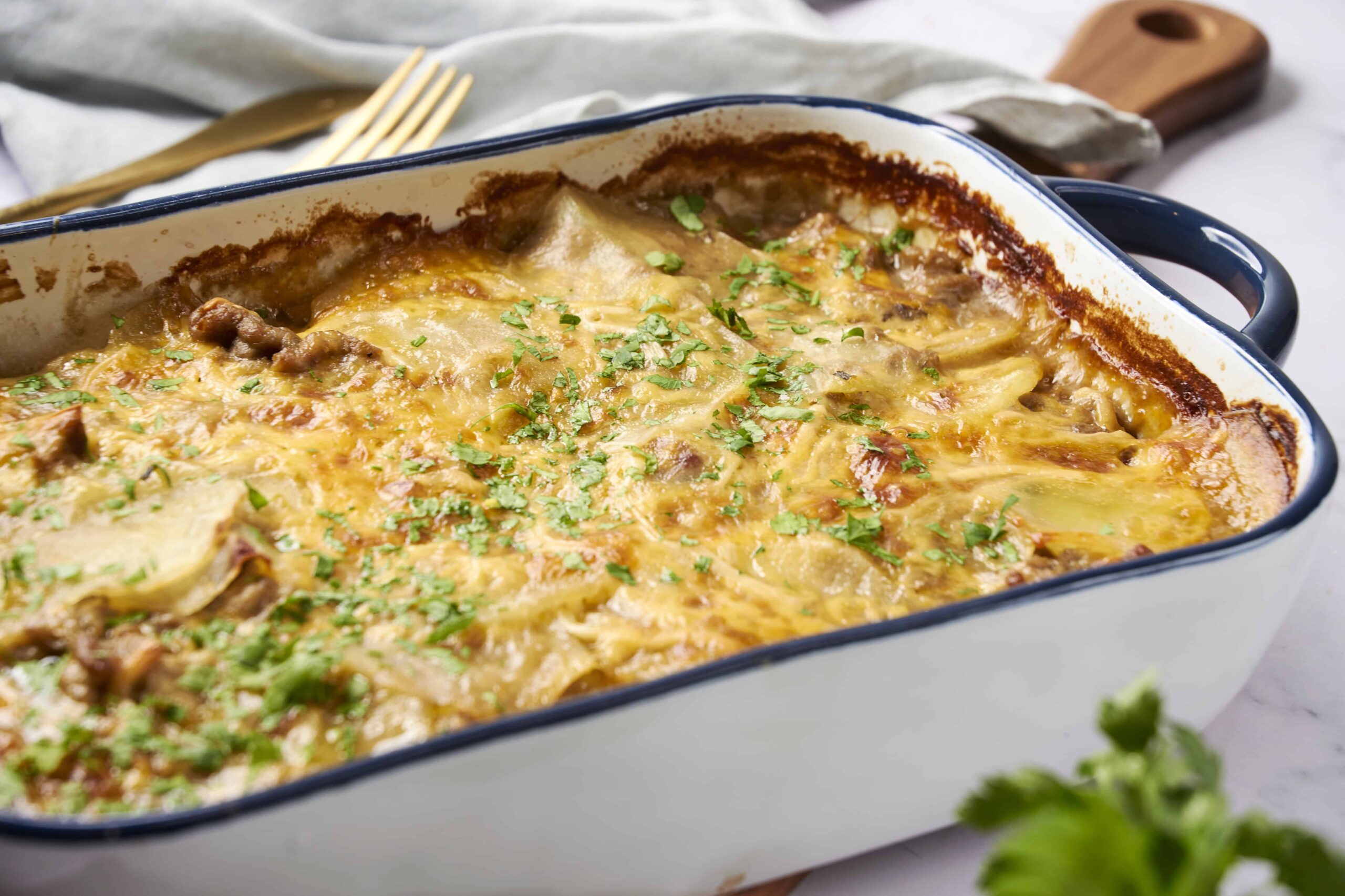 Golden baked cheesy beef and pasta casserole in a white and blue baking dish, topped with fresh chopped herbs.