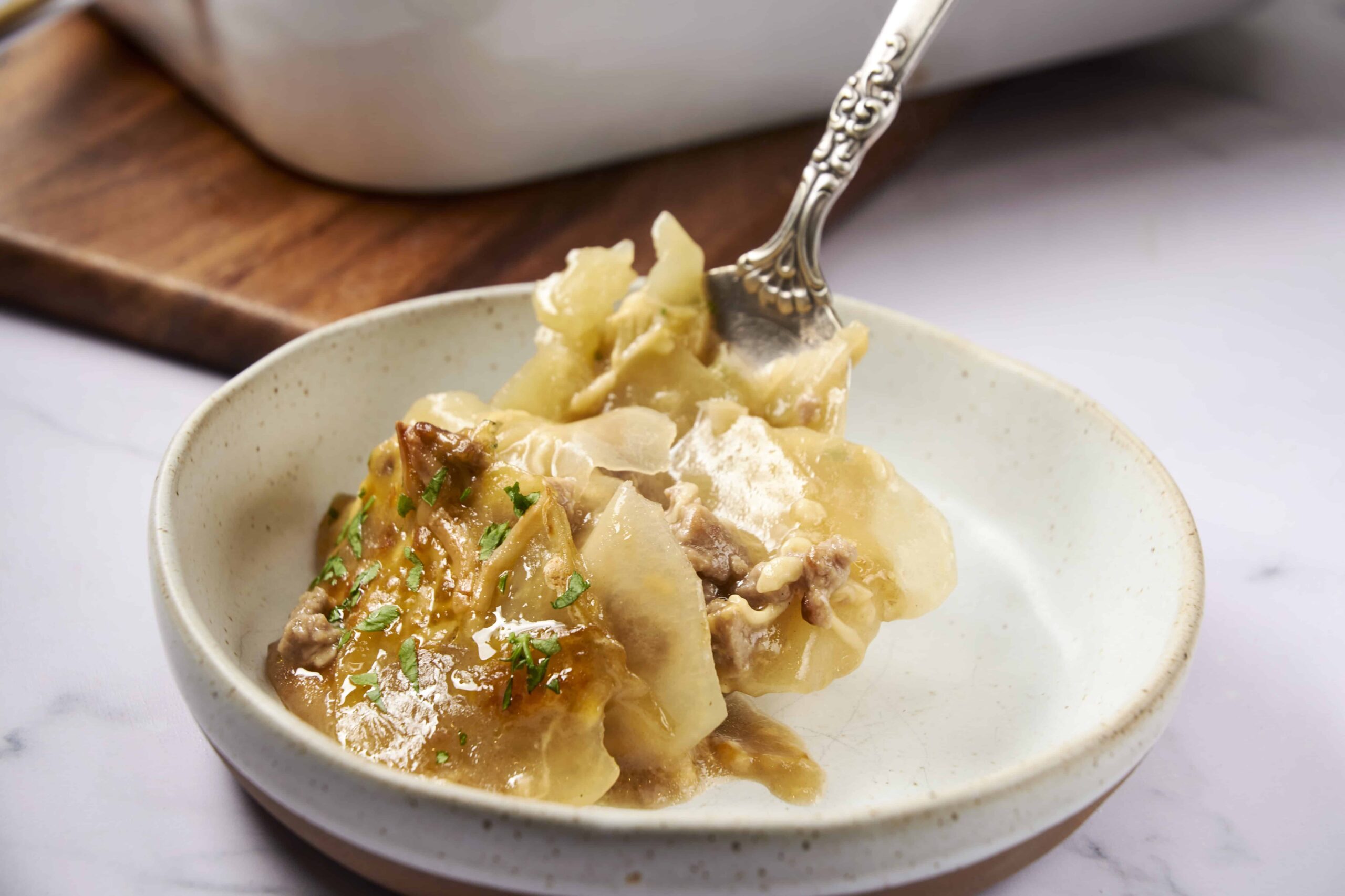 Savory beef and potato pierogi served with herbs on an off-white ceramic plate, featuring a silver fork for easy serving. Perfect comfort food, highlighting traditional Polish cuisine.
