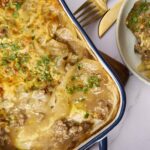 Creamy pot pie with tender beef, potatoes, and melted cheese topped with fresh parsley in a blue-rimmed dish.