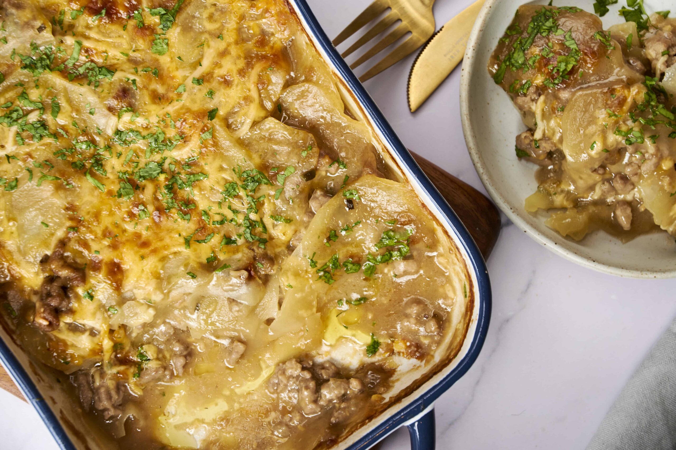 Creamy pot pie with tender beef, potatoes, and melted cheese topped with fresh parsley in a blue-rimmed dish.