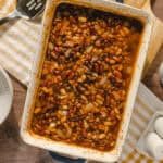 Hearty baked beans casserole with black beans, kidney beans, and onions in a savory sauce on a wooden table.
