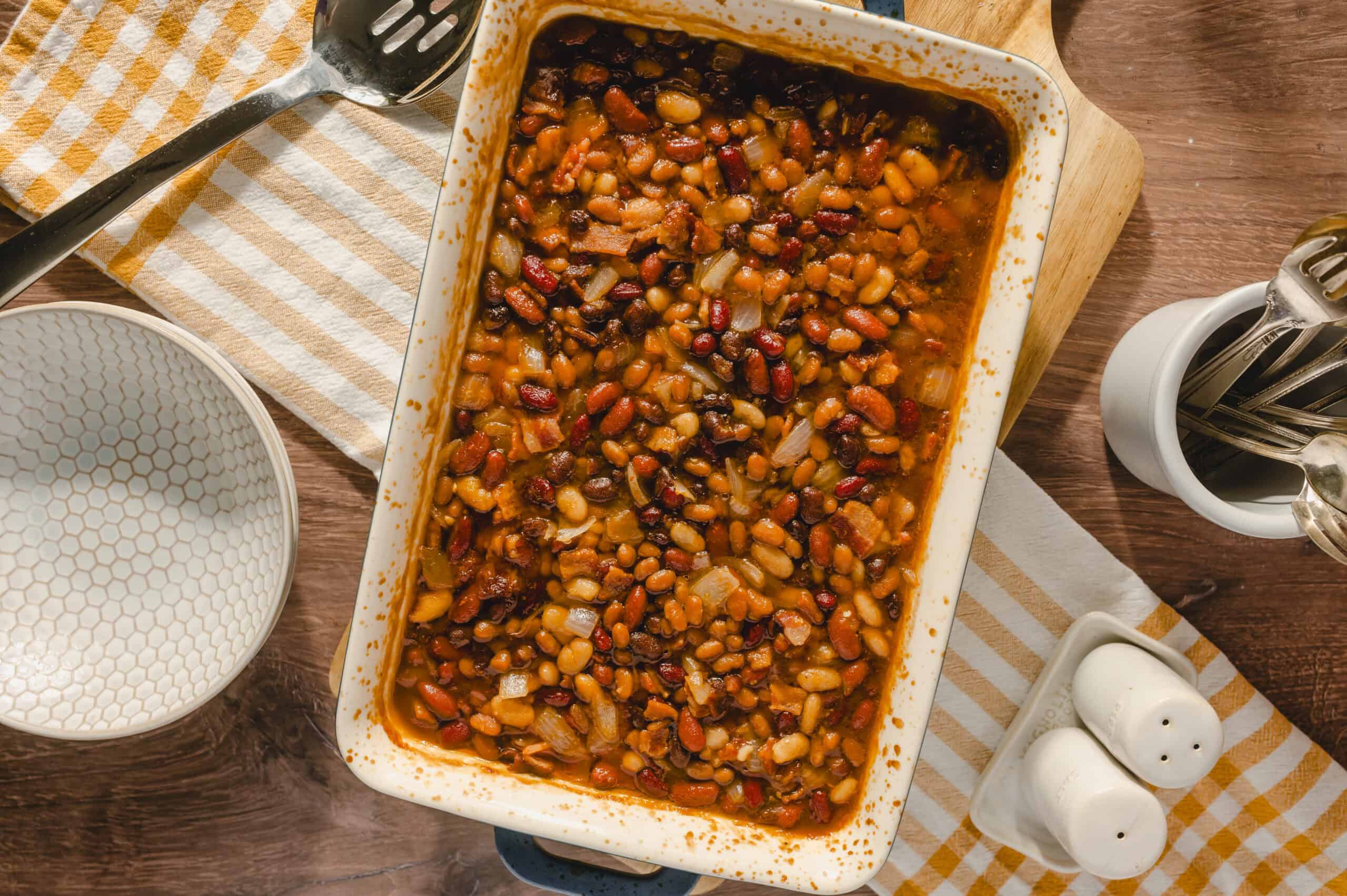 Hearty baked beans casserole with black beans, kidney beans, and onions in a savory sauce on a wooden table.