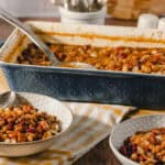 Hearty baked bean casserole served in a vintage baking dish with two bowls of the cooked beans on a rustic table.