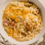 Creamy sausage and cheese potato hash casserole, with shredded cheddar and melted cheese, served on a white plate. Perfect comfort food for breakfast or brunch with sausage slices.