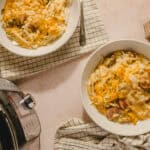 Creamy sausage and cheese pasta baked in a slow cooker, served in white bowls on checkered napkins, with a fork and spoon placed nearby, perfect for a comforting home-cooked meal.