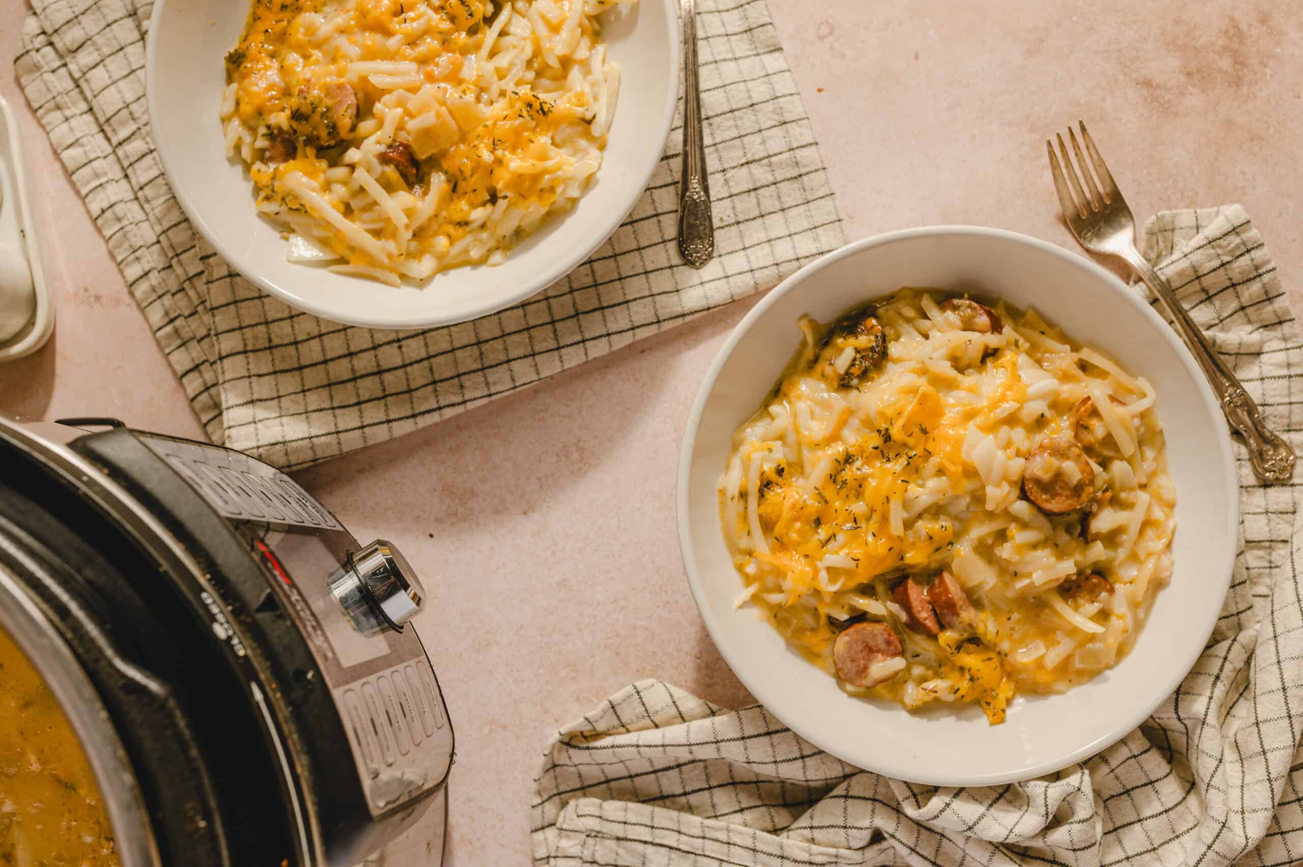 Creamy sausage and cheese pasta baked in a slow cooker, served in white bowls on checkered napkins, with a fork and spoon placed nearby, perfect for a comforting home-cooked meal.