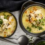 Creamy chicken and vegetable soup in black bowls with shredded cheese and fresh herbs, served as comfort food for cold days.