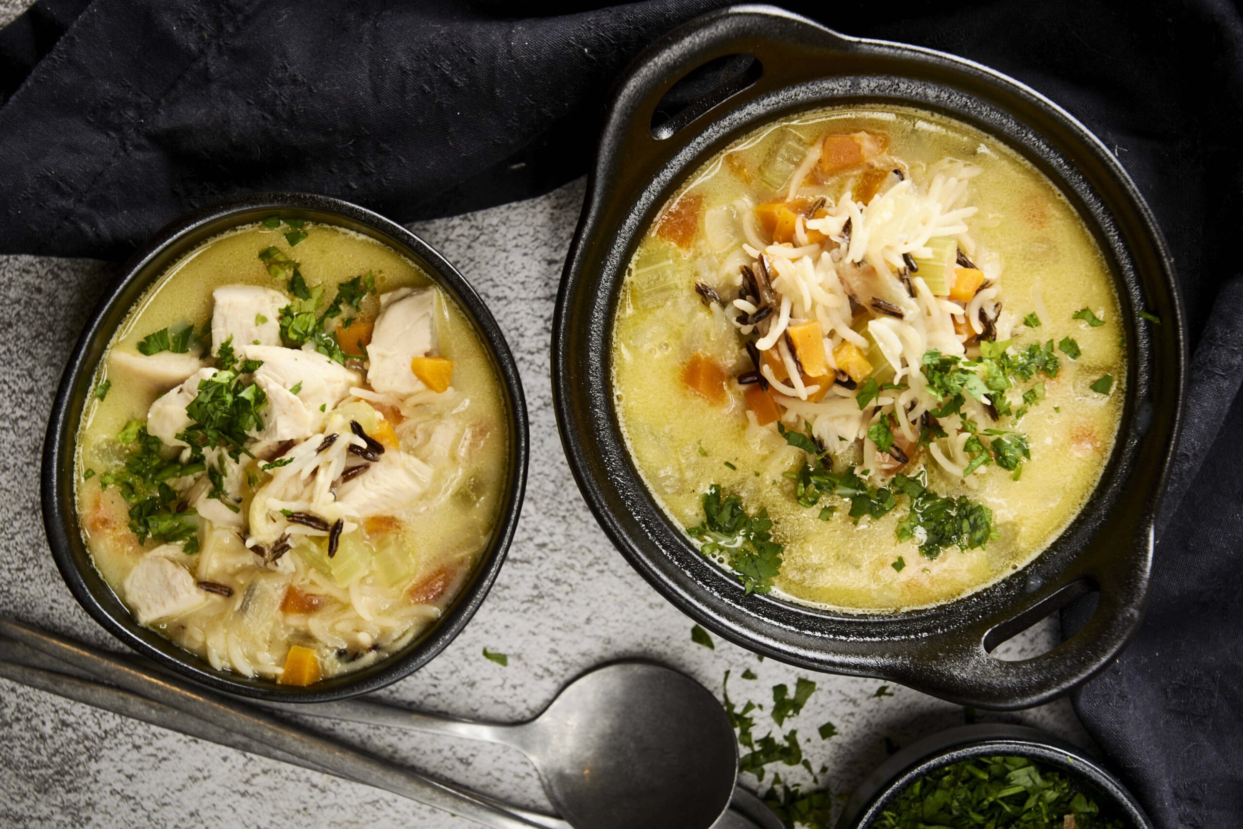Creamy chicken and vegetable soup in black bowls with shredded cheese and fresh herbs, served as comfort food for cold days.