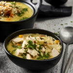 Savory chicken and vegetable soup with herbs in black bowls, cozy comfort food, hearty homemade soup with shredded chicken, carrots, herbs, and noodles, perfect for winter meals and family dinners.