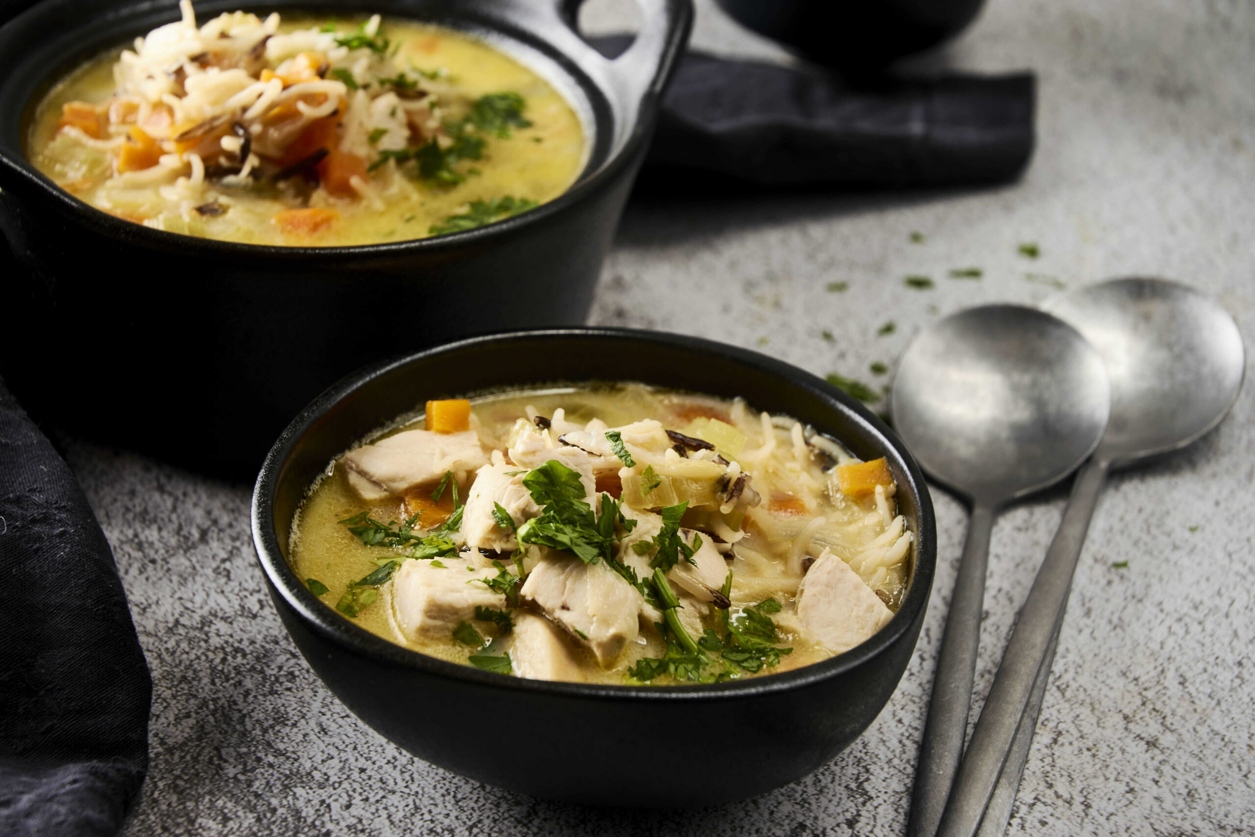 Savory chicken and vegetable soup with herbs in black bowls, cozy comfort food, hearty homemade soup with shredded chicken, carrots, herbs, and noodles, perfect for winter meals and family dinners.