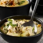 Comforting chicken and rice soup in a black bowl with fresh herbs and vegetables, served with black bowls and a spoon. Ideal for cozy home-cooked meal recipes and healthy comfort food ideas.