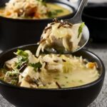Creamy chicken and mushroom soup served in a black bowl with fresh herbs and noodles, ready to enjoy for a comforting meal.