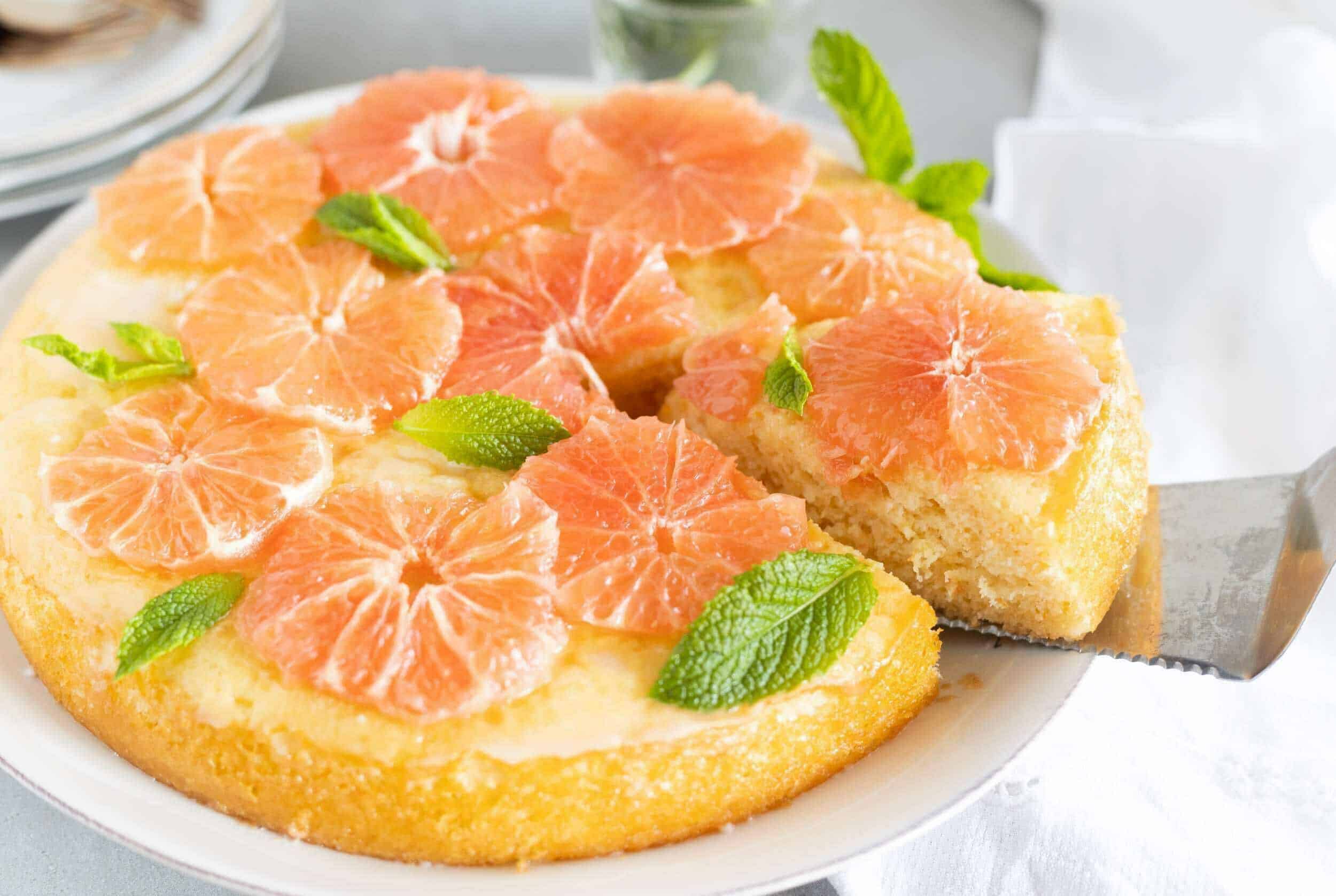 Freshly baked citrus cake topped with sliced mandarins and mint leaves, served on a white plate, perfect for summer desserts and citrus lovers.