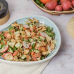 Fresh veggie salad with radishes, cucumbers, and crushed tortilla chips served in a white bowl on a light surface.