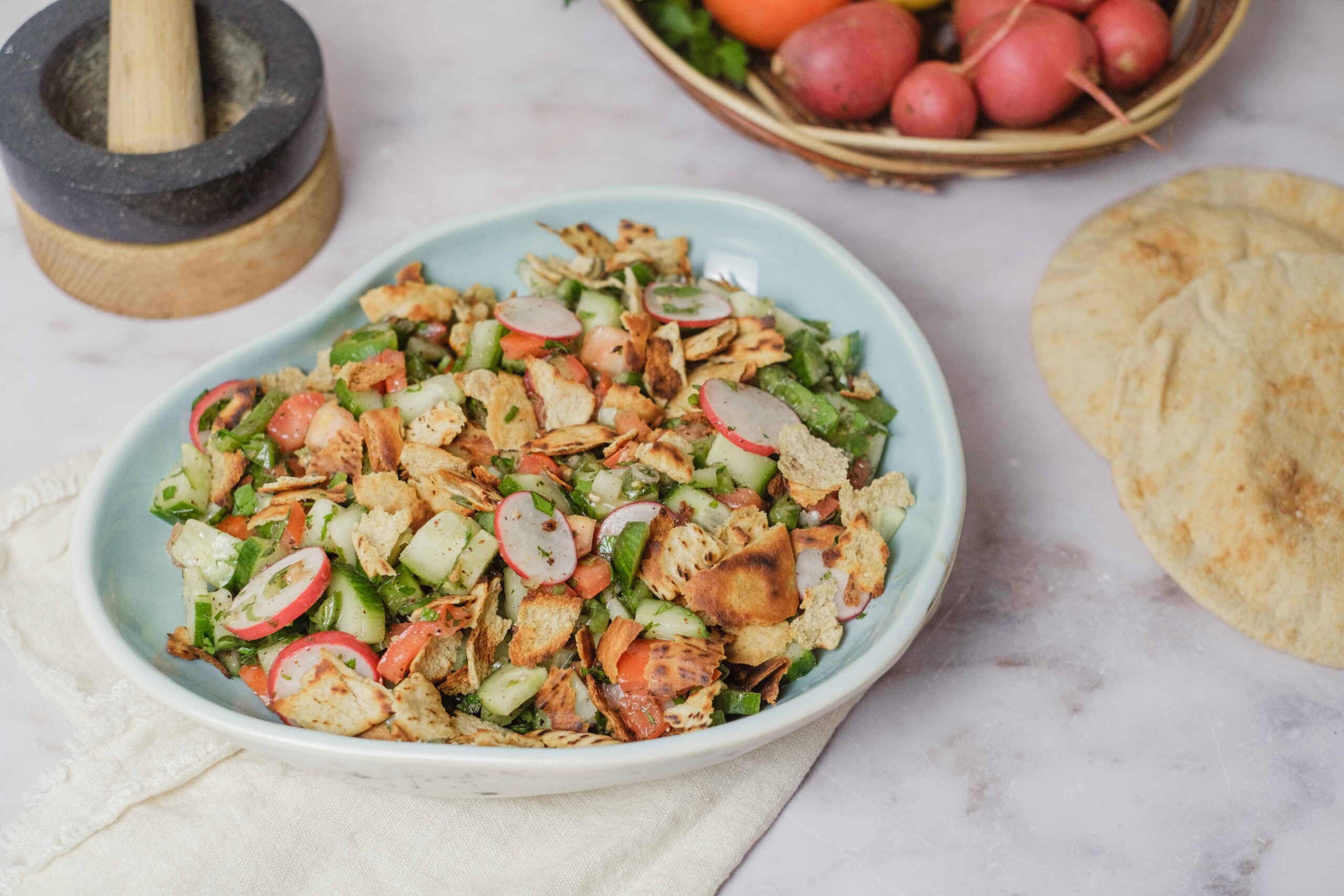 Fresh veggie salad with radishes, cucumbers, and crushed tortilla chips served in a white bowl on a light surface.