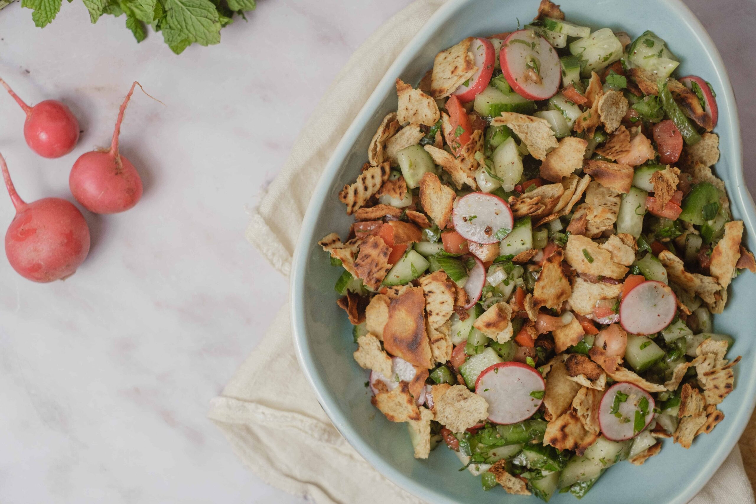 Grilled chicken salad with radishes, cucumbers, and fresh herbs in a white bowl on a cozy cloth, surrounded by radishes on marble surface, perfect for healthy recipes and summer meals.