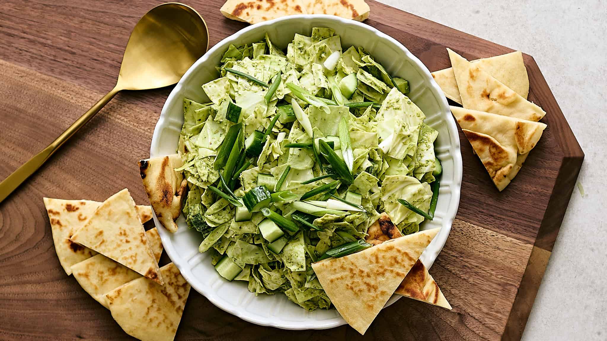 Fresh green vegetable salad with chopped lettuce, cucumber, and green onion served with toasted pita bread on wooden cutting board. Perfect healthy side dish or appetizer.
