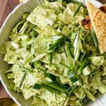 Fresh chopped green cabbage salad with green onions and toasted flatbread in a white bowl, served on a wooden surface.
