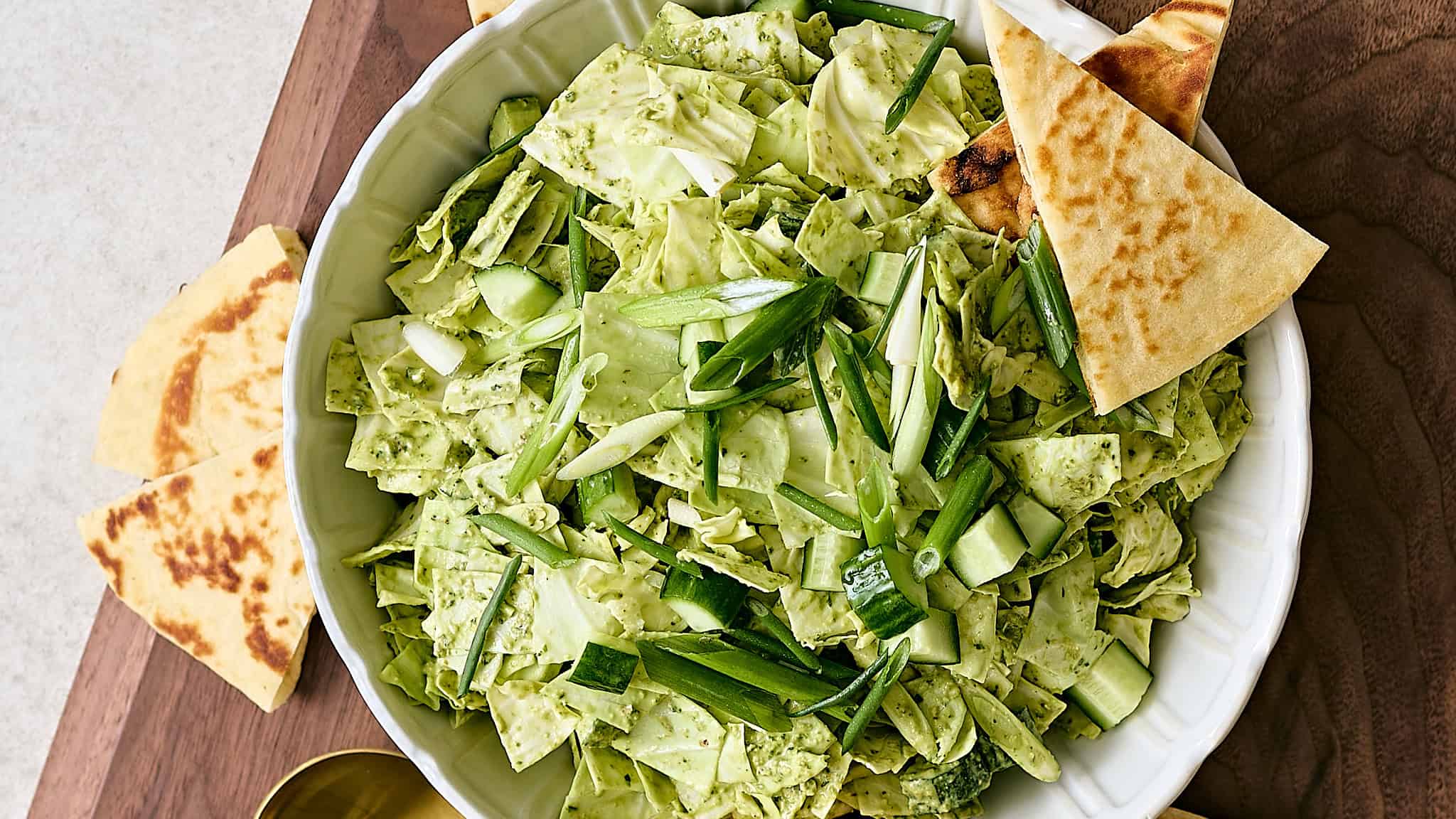 Fresh chopped green cabbage salad with green onions and toasted flatbread in a white bowl, served on a wooden surface.