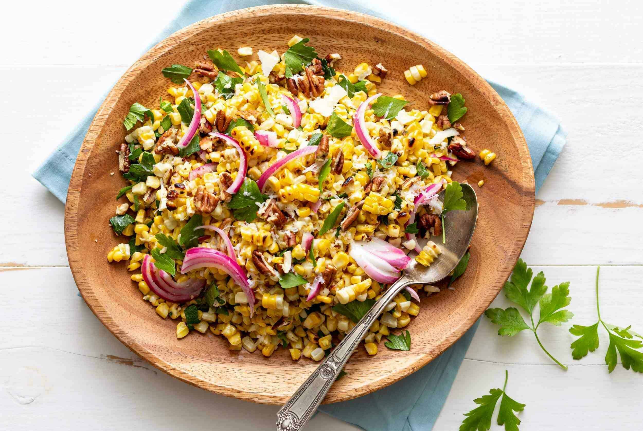 Bright colorful corn salad with red onions, fresh herbs, and chopped pecans on a wooden plate, ideal for summer meals or healthy recipes.
