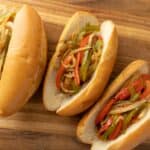 Sliced hoagie sandwiches filled with sautéed bell peppers and onions, placed on a wooden cutting board. Perfect for flavorful sandwiches or appetizer recipes.