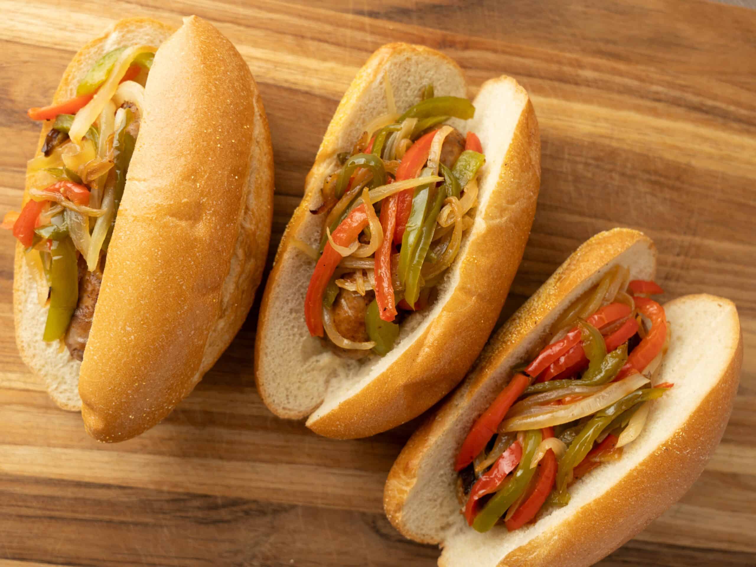 Sliced hoagie sandwiches filled with sautéed bell peppers and onions, placed on a wooden cutting board. Perfect for flavorful sandwiches or appetizer recipes.