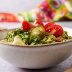 Fresh guacamole with diced tomatoes, pickled jalapeños, chopped cilantro, and avocado in a white ceramic bowl, perfect for serving as a healthy snack or appetizer.