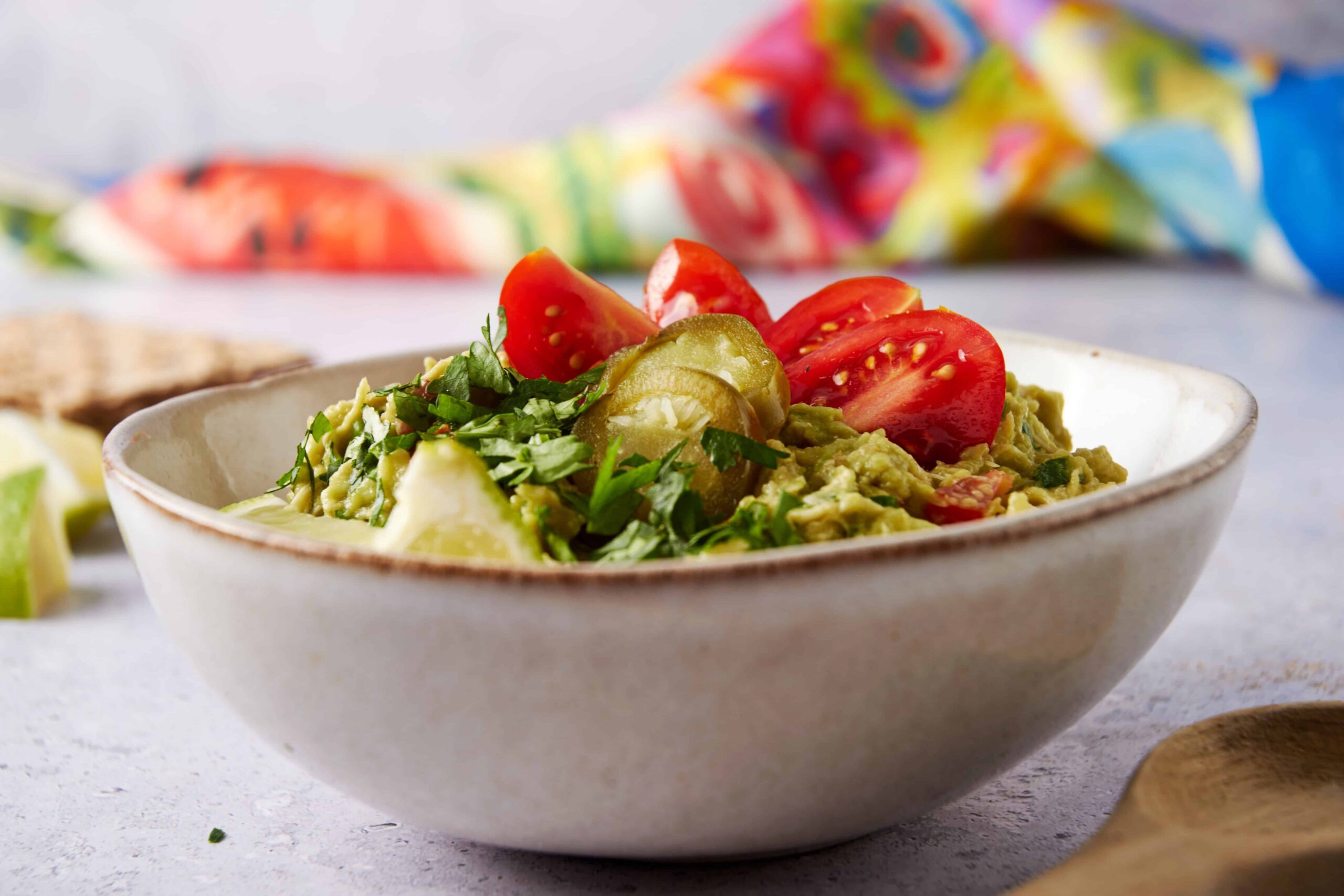 Fresh guacamole with diced tomatoes, pickled jalapeños, chopped cilantro, and avocado in a white ceramic bowl, perfect for serving as a healthy snack or appetizer.