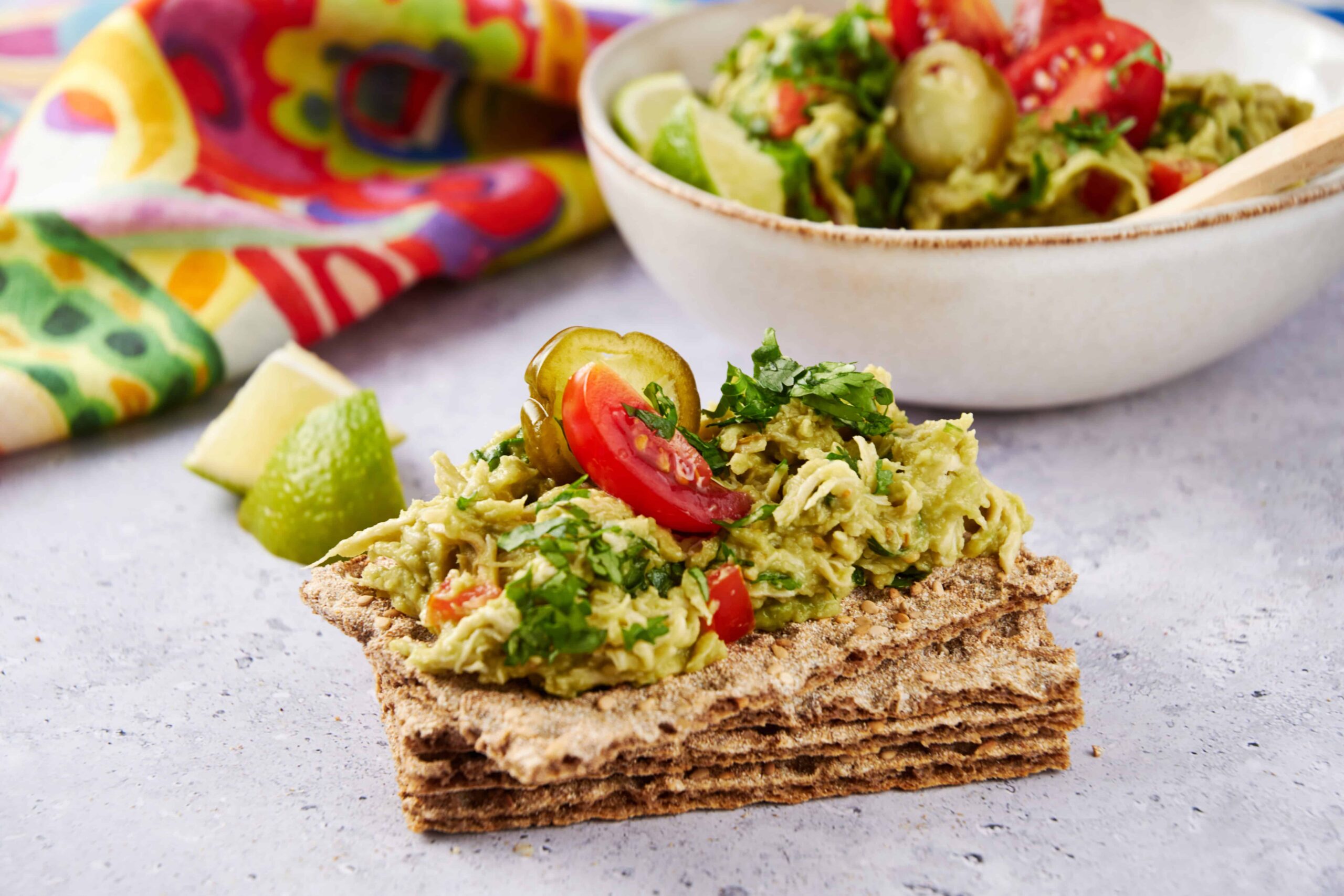 Creamy avocado and tomato spread on whole grain crispbread with fresh lime and cilantro garnish, served as a healthy snack or appetizer. Perfect for avocado lovers and nutritious snacks.