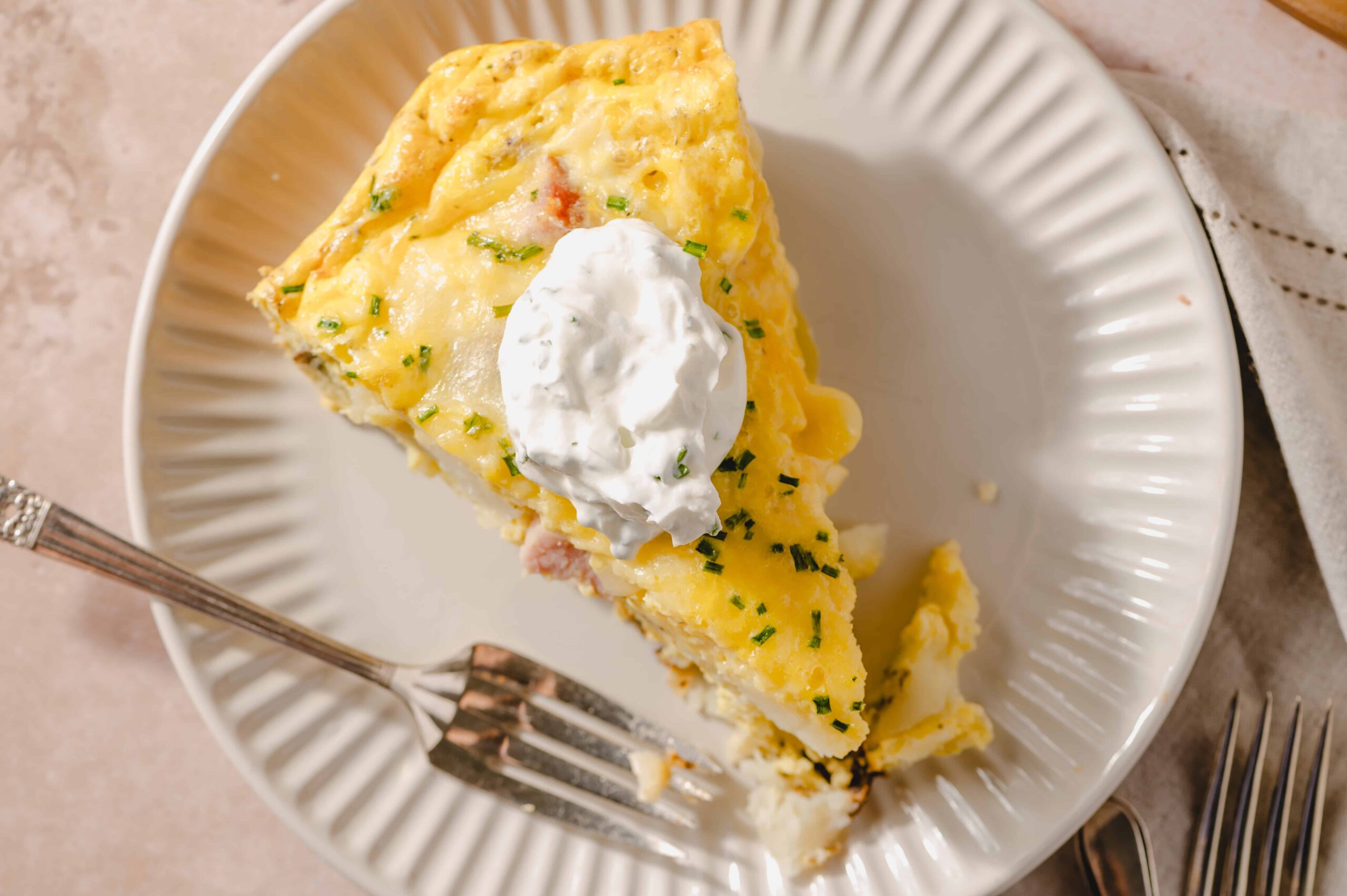 Creamy ham and cheese breakfast casserole topped with whipped cream on a white plate, served with silver forks, perfect for brunch or hearty breakfast.