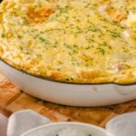 Creamy breakfast casserole with cheese, eggs, and ham topped with chopped herbs, baked until golden and bubbling for a hearty morning meal.