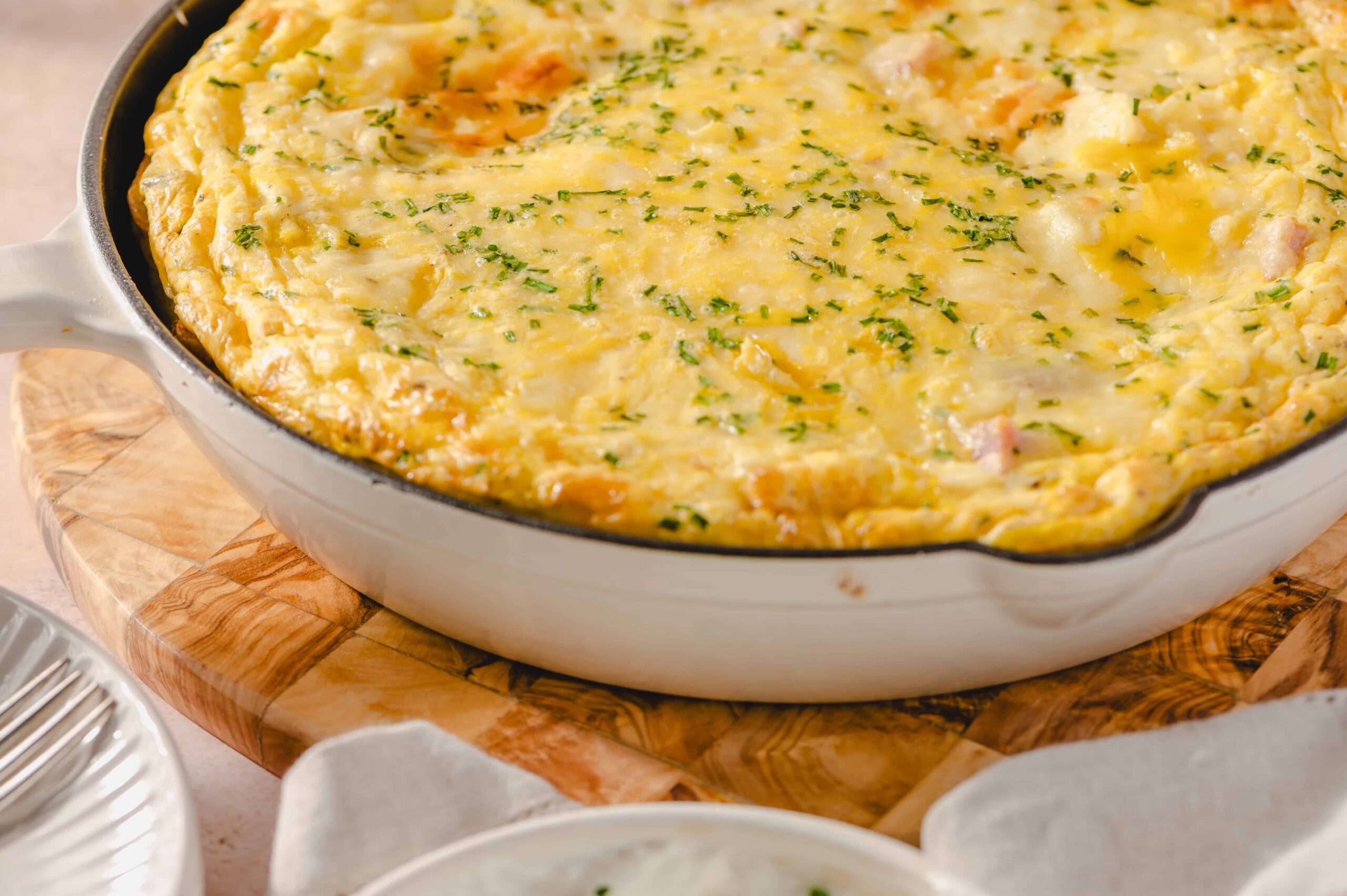 Creamy breakfast casserole with cheese, eggs, and ham topped with chopped herbs, baked until golden and bubbling for a hearty morning meal.