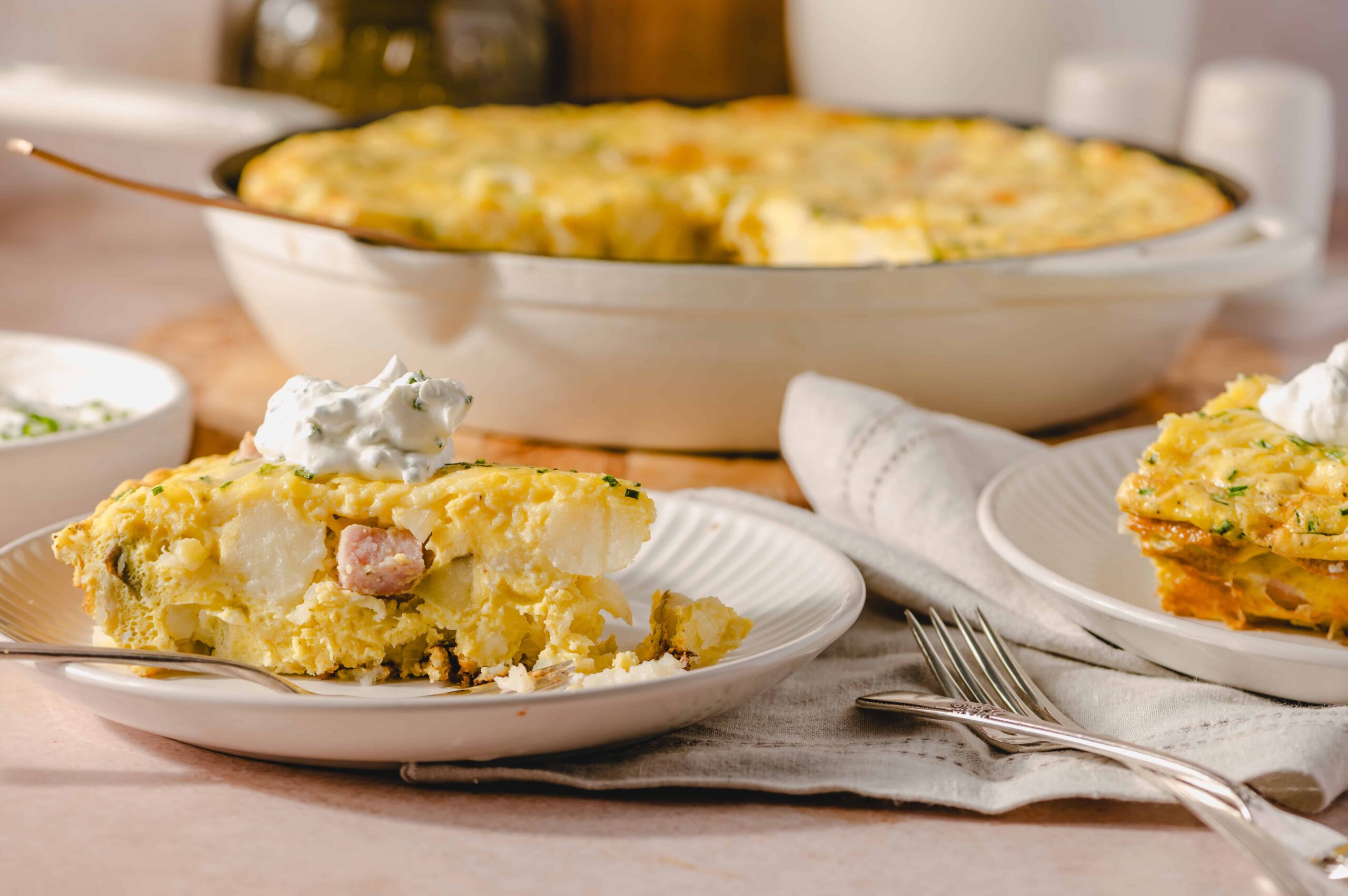 Creamy potato and ham casserole served with sour cream on a white plate, featuring a baked golden crust and melted cheese, perfect for comforting family meals.