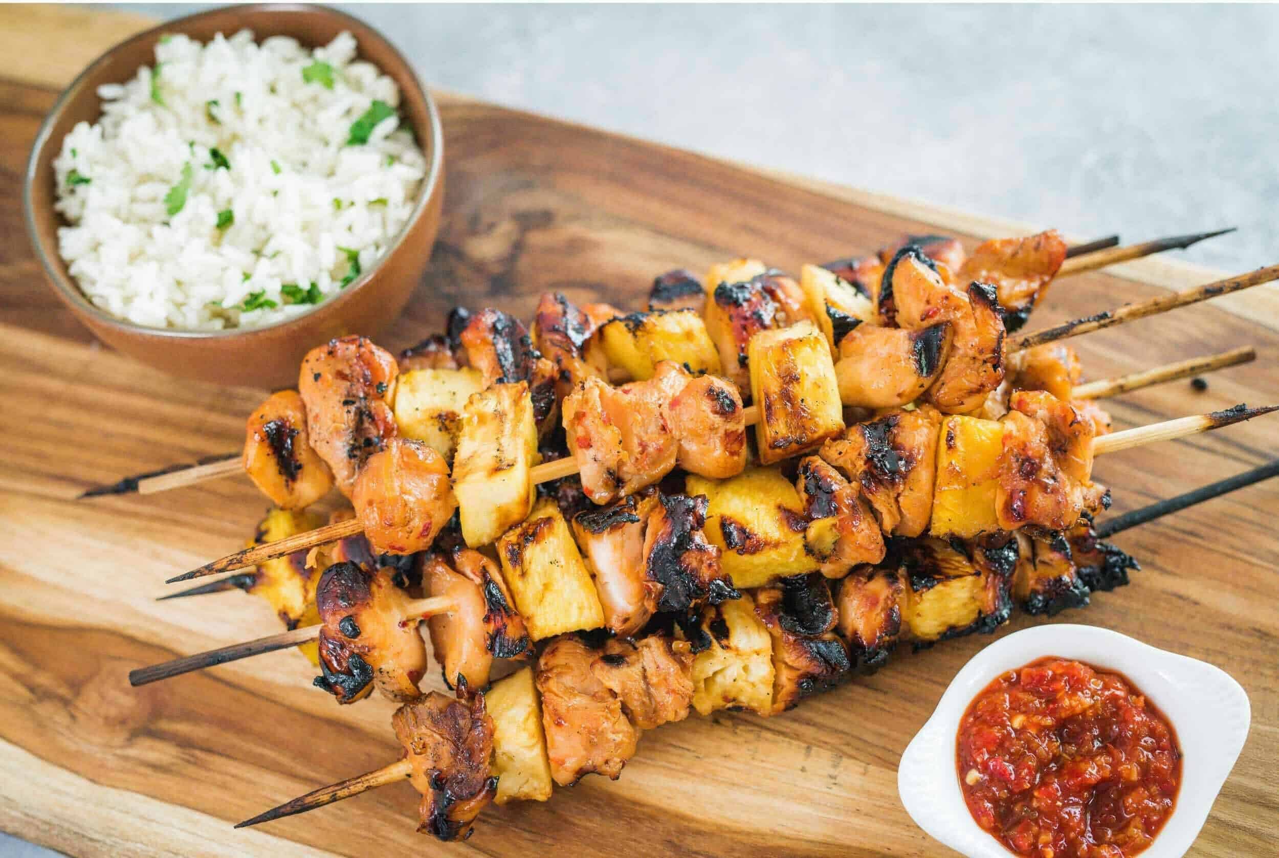Juicy grilled chicken and pineapple skewers served with a side of cilantro lime rice and spicy salsa on a wooden platter. Perfect for BBQ, outdoor dining, or summer cookouts.